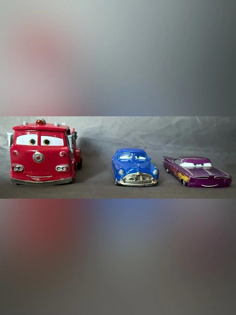 Disney Pixar Cars Diecast: Red Fire Truck, Doc Hudson, and Purple Ramon.